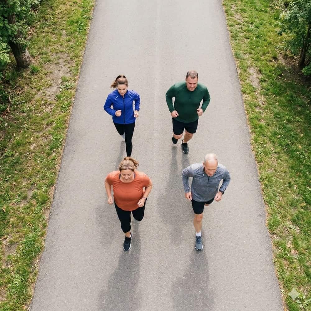 Seitenstechen beim Laufen: Ursachen, Soforthilfe & Prävention 3 Vier Läufer verschiedenen Alters aus Vogelperspektive auf Parkweg bei gemeinsamem regelmäßigem Training
